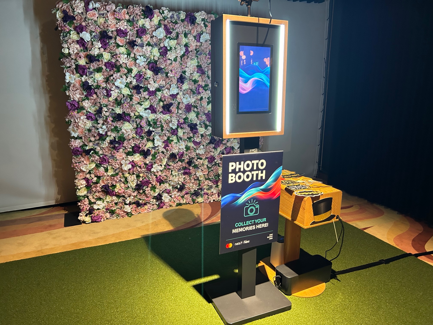 El fotomatón de Costa Photo Booth junto a una pared de flores, con las impresiones listas para los invitados